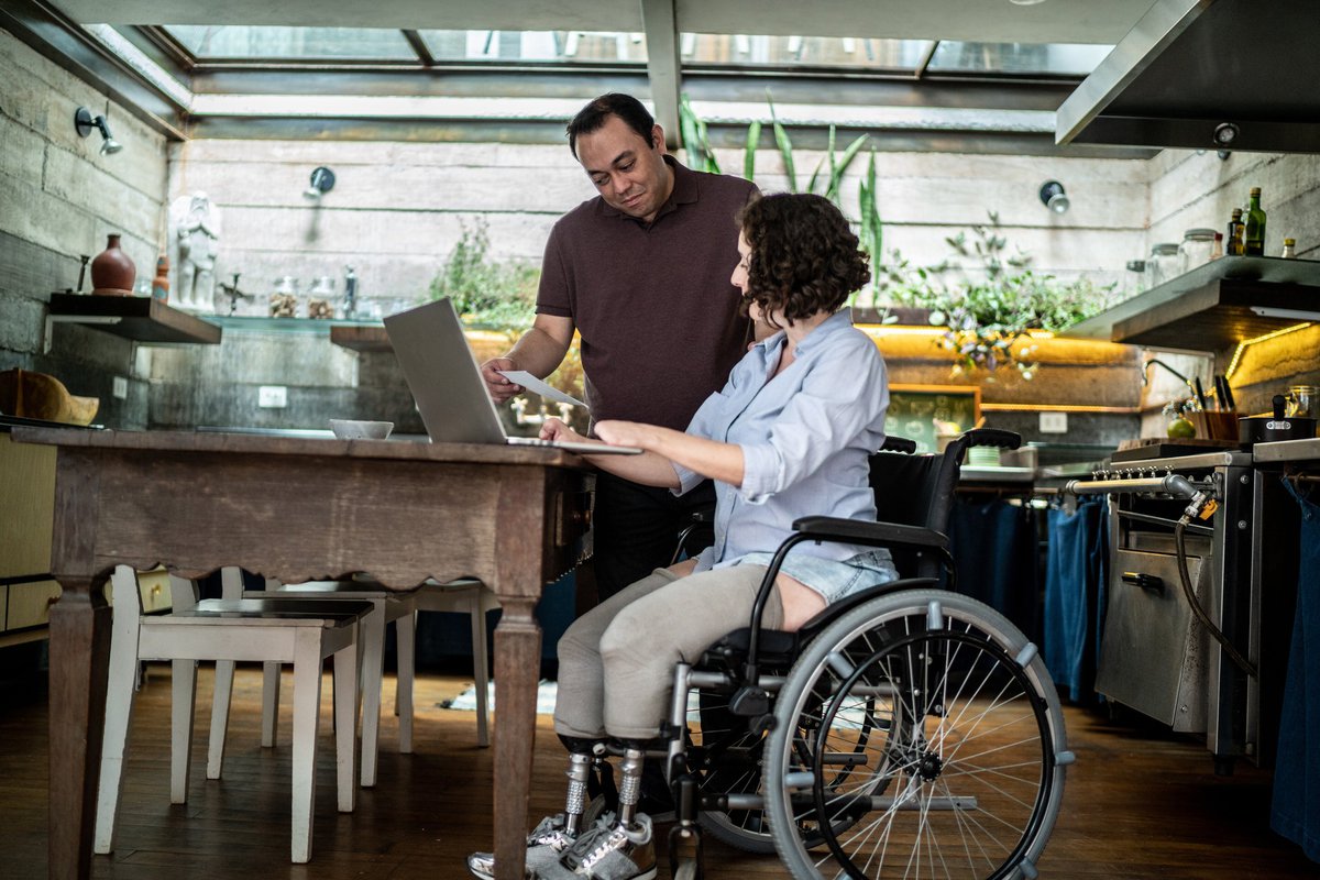 An interabled couple looks at a laptop together at their kitchen table.