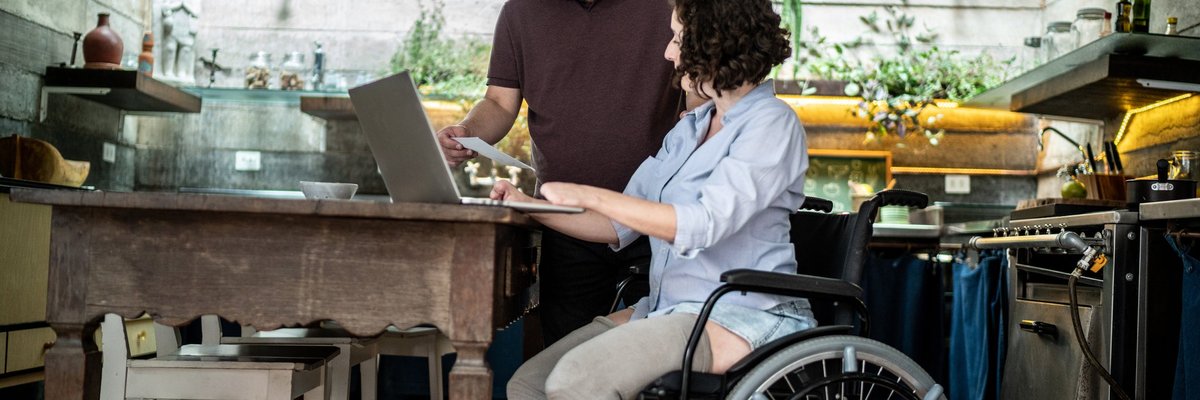 A couple smiles while looking at their laptop in their kitchen.