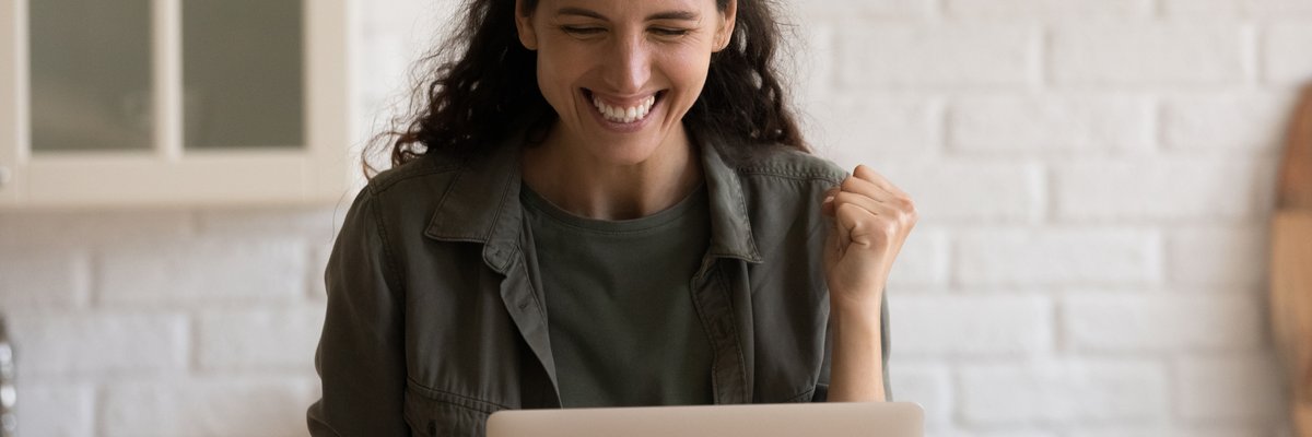 An adult looks at something exciting on their laptop and pumps their fist in the air.