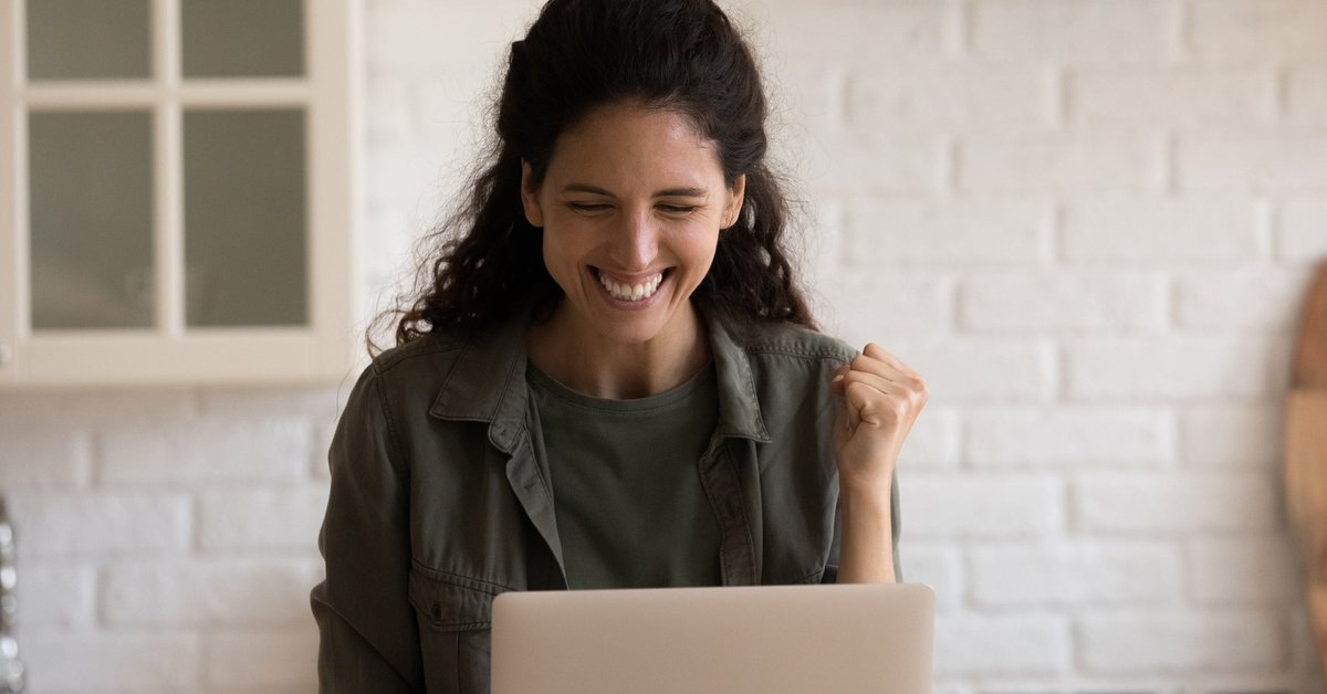 An adult looks at something exciting on their laptop and pumps their fist in the air.