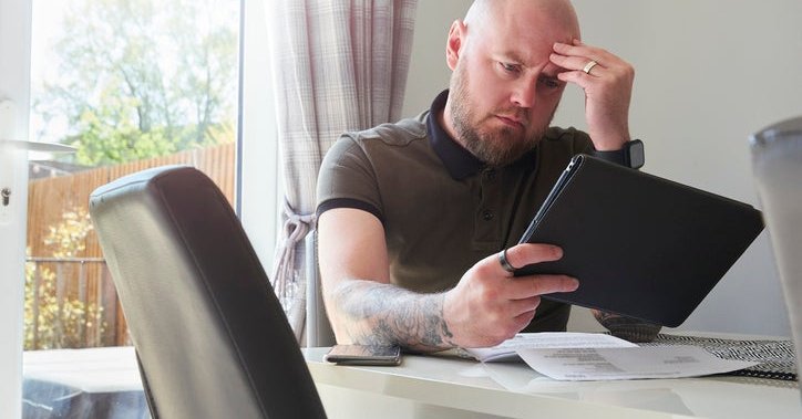 A homeowner looks worried as he reads through his household bills at the dining table.