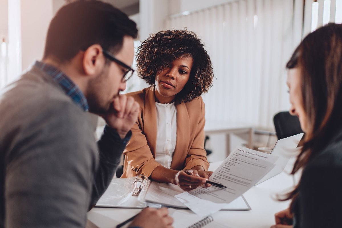 A couple decides whether to sign a mortgage agreement or not while sitting at a desk in a bank.