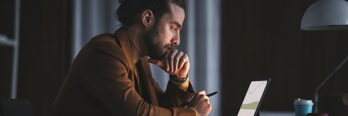 A pensive person reads a graph on a laptop in an office late at night.