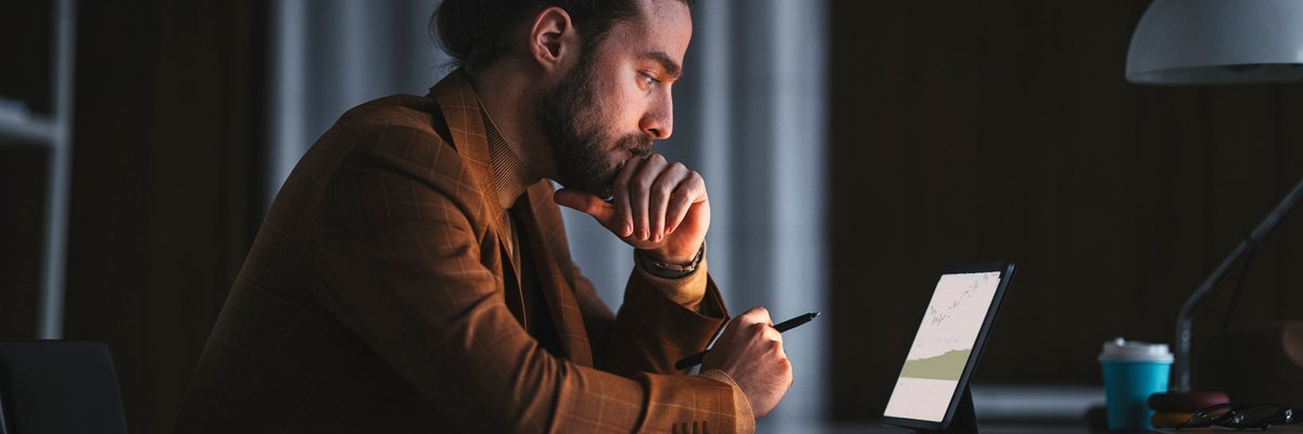 A pensive person reads a graph on a laptop in an office late at night.