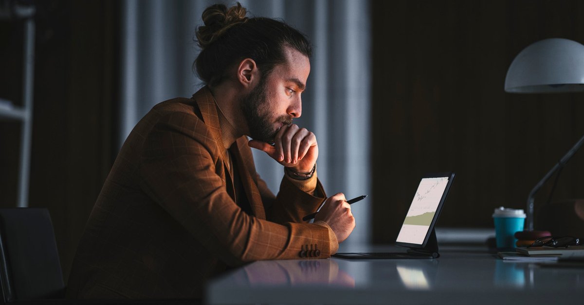 A pensive person reads a graph on a laptop in an office late at night.