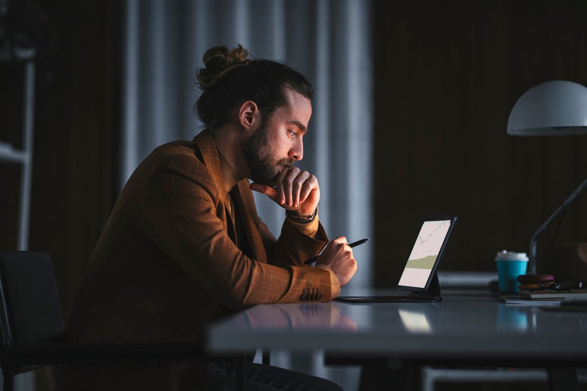 A pensive person reads a graph on a laptop in an office late at night.