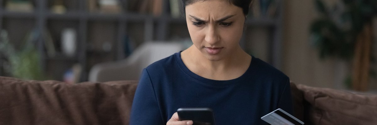 Someone frowns at their smartphone while holding up their credit card.