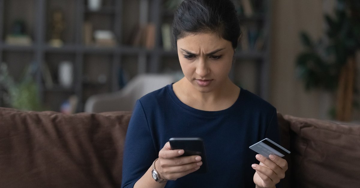 Someone frowns at their smartphone while holding up their credit card.
