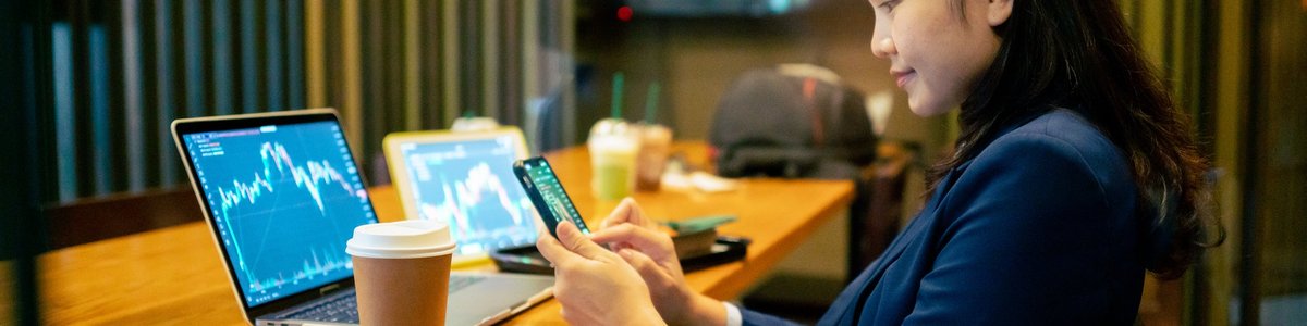 A smiling adult trades stocks using their mobile devices in a coffee shop.