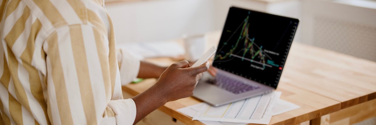 A person analyzes a cryptocurrency graph on their laptop in their kitchen.