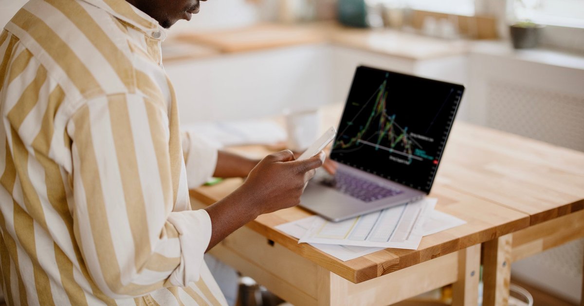 A person analyzes a cryptocurrency graph on their laptop in their kitchen.