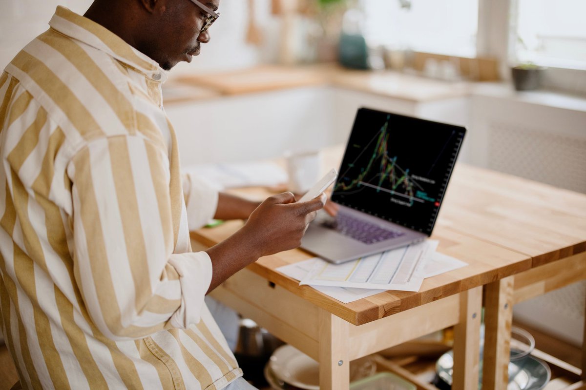 A person analyzes a cryptocurrency graph on their laptop in their kitchen.