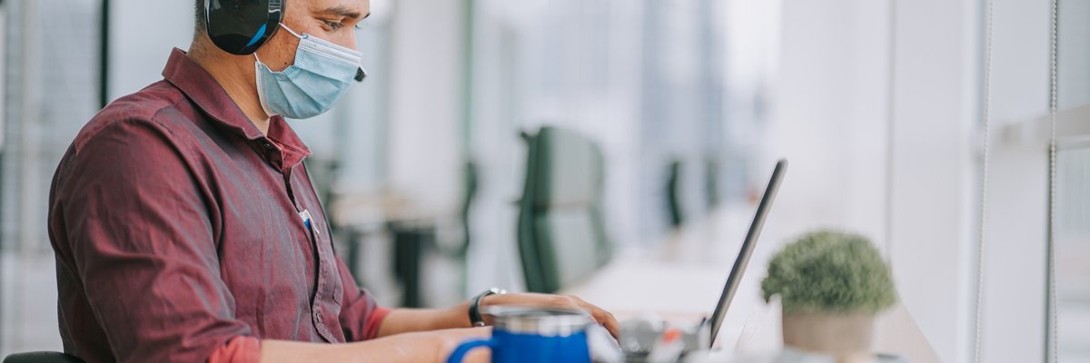 A worker wearing a mask and using a wheelchair works on a laptop.