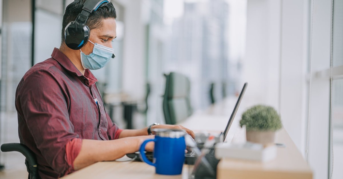 A worker wearing a mask and using a wheelchair works on a laptop.