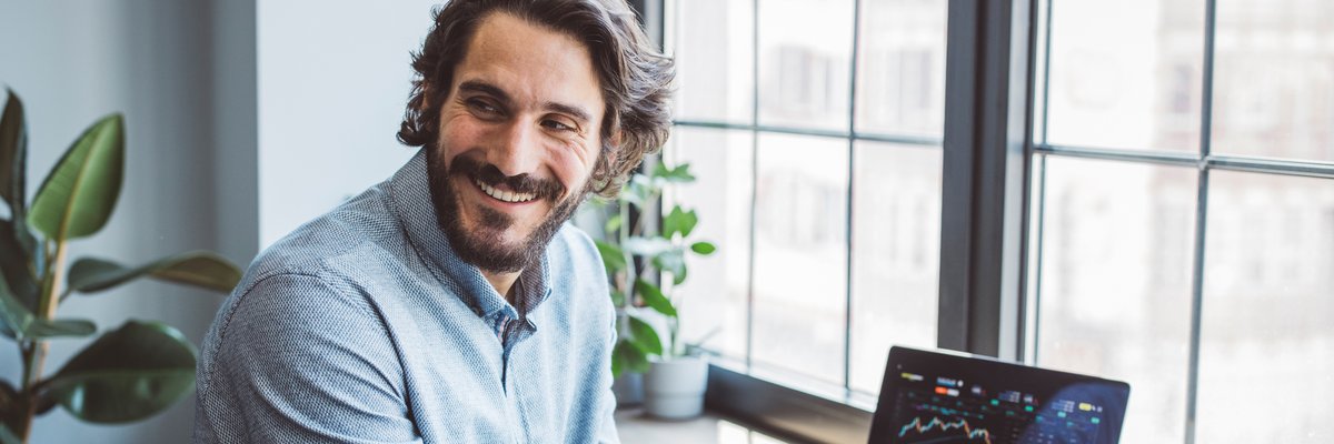A businessperson smiles as they view crypto graphs on a laptop from home.