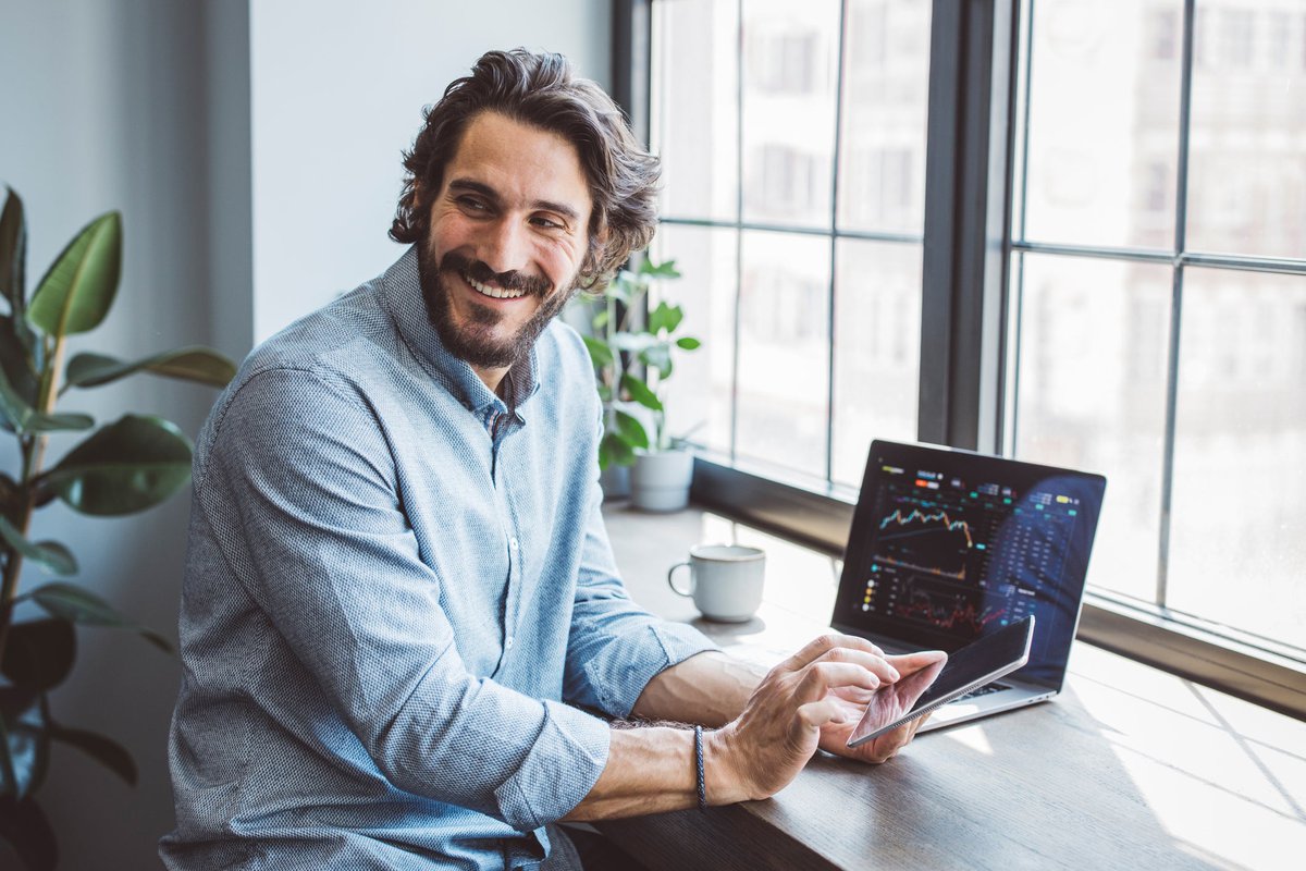 A businessperson smiles as they view crypto graphs on a laptop from home.