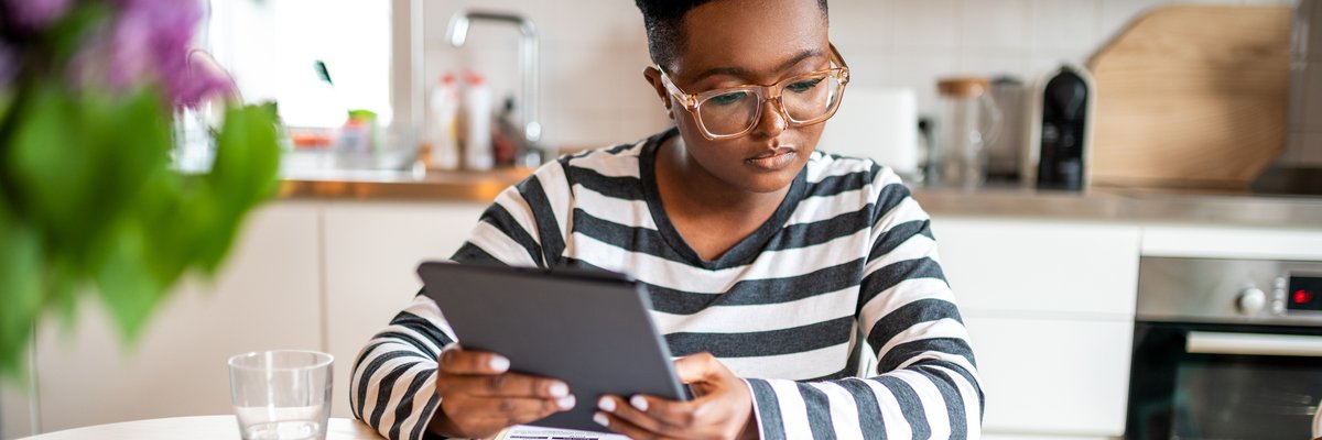 A person looks over paperwork and uses a tablet in their kitchen.