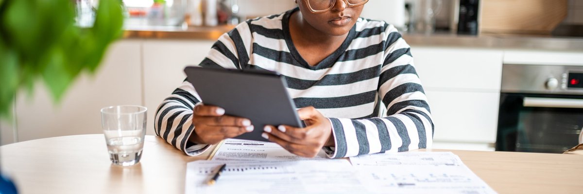 A person looks over paperwork and uses a tablet in their kitchen.