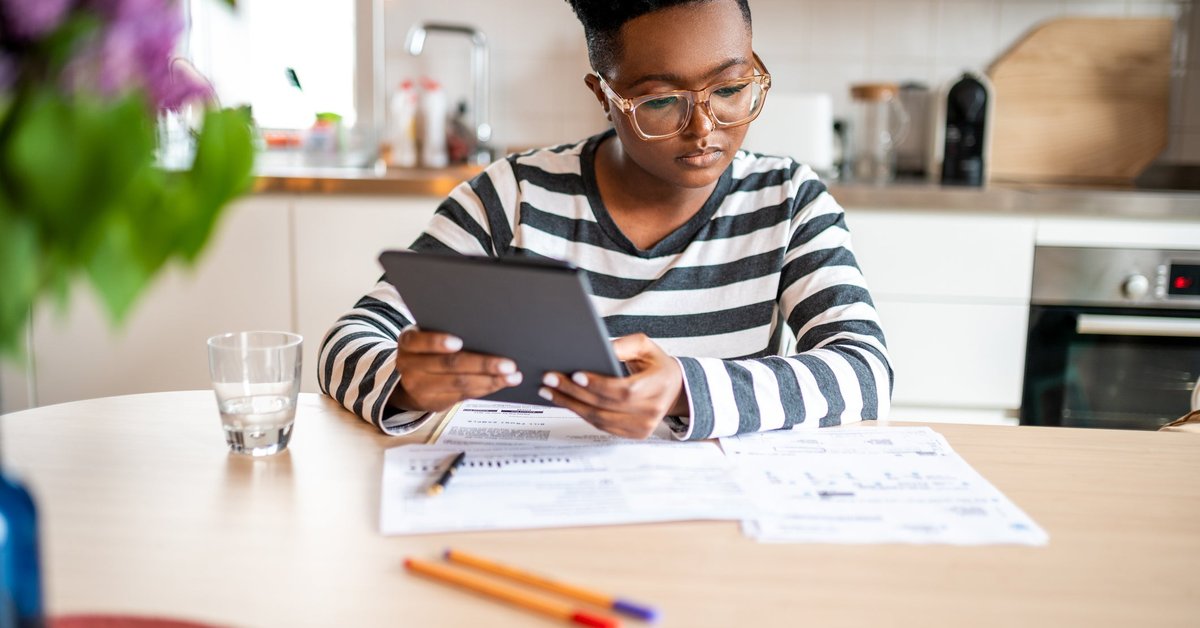 A person looks over paperwork and uses a tablet in their kitchen.