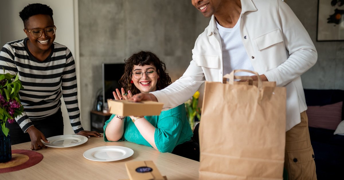 A group of young adults excitedly unpack their food delivery order in their kitchen.