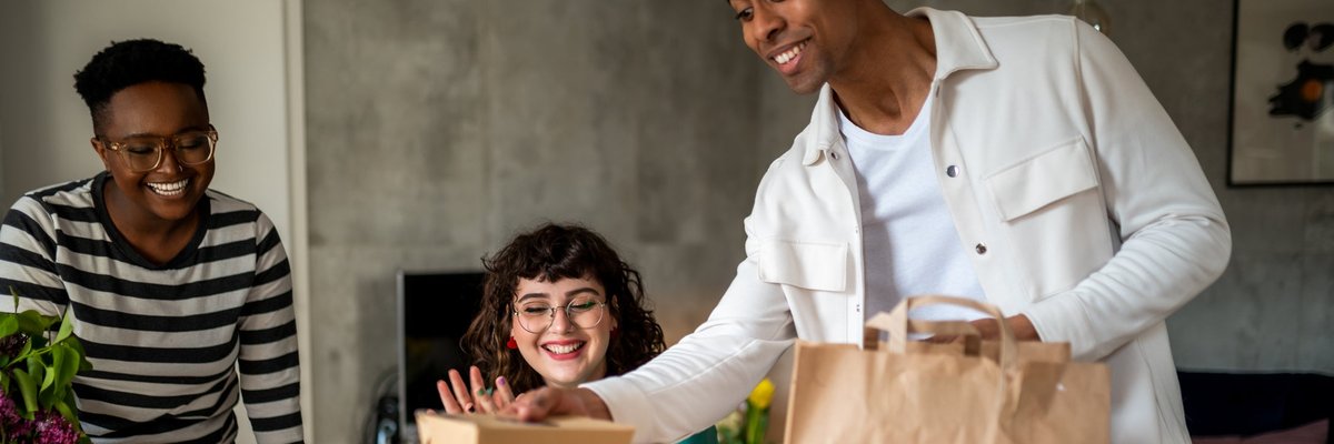 A group of young adults excitedly unpack their food delivery order in their kitchen.