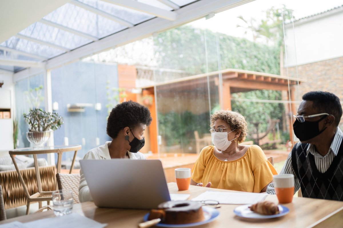 A business professional meets with a couple in their home while pointing at a laptop.