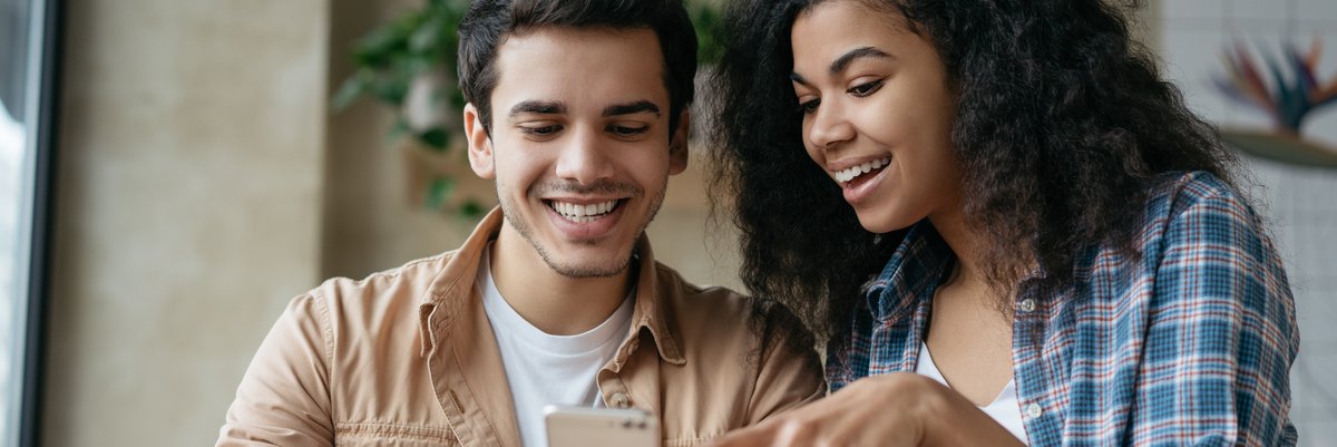 Couple smiling while reviewing something on smartphone screen.