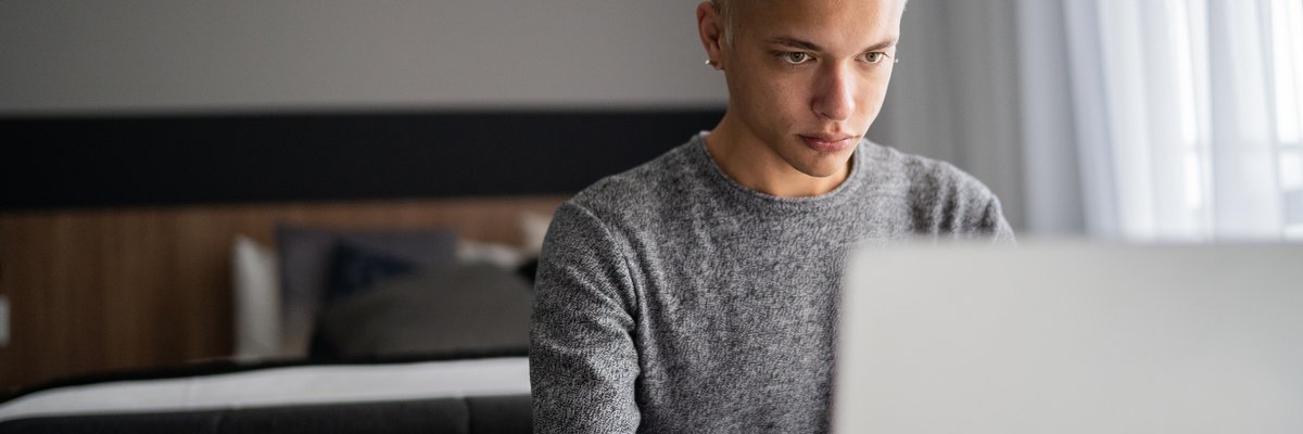 A young adult uses their laptop at home during breakfast.