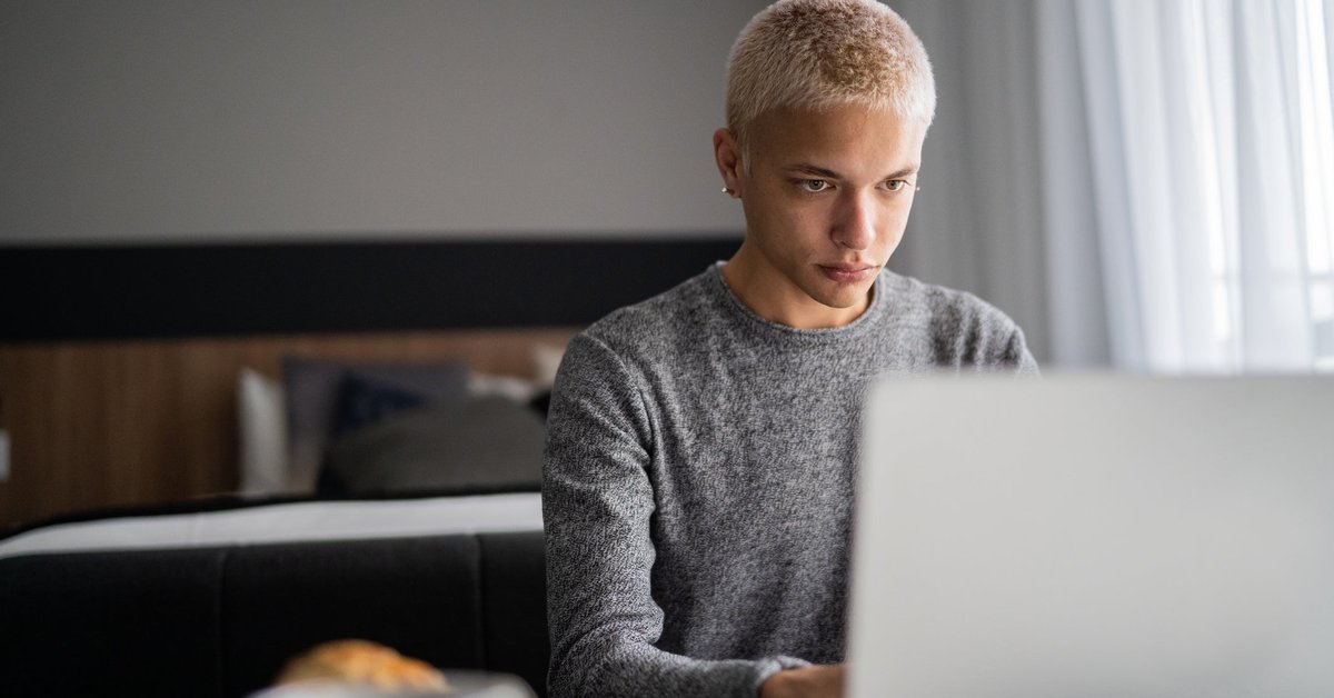 A young adult uses their laptop at home during breakfast.