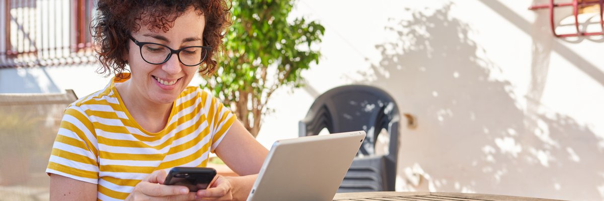Person smiling using tablet and phone while sitting outdoors.
