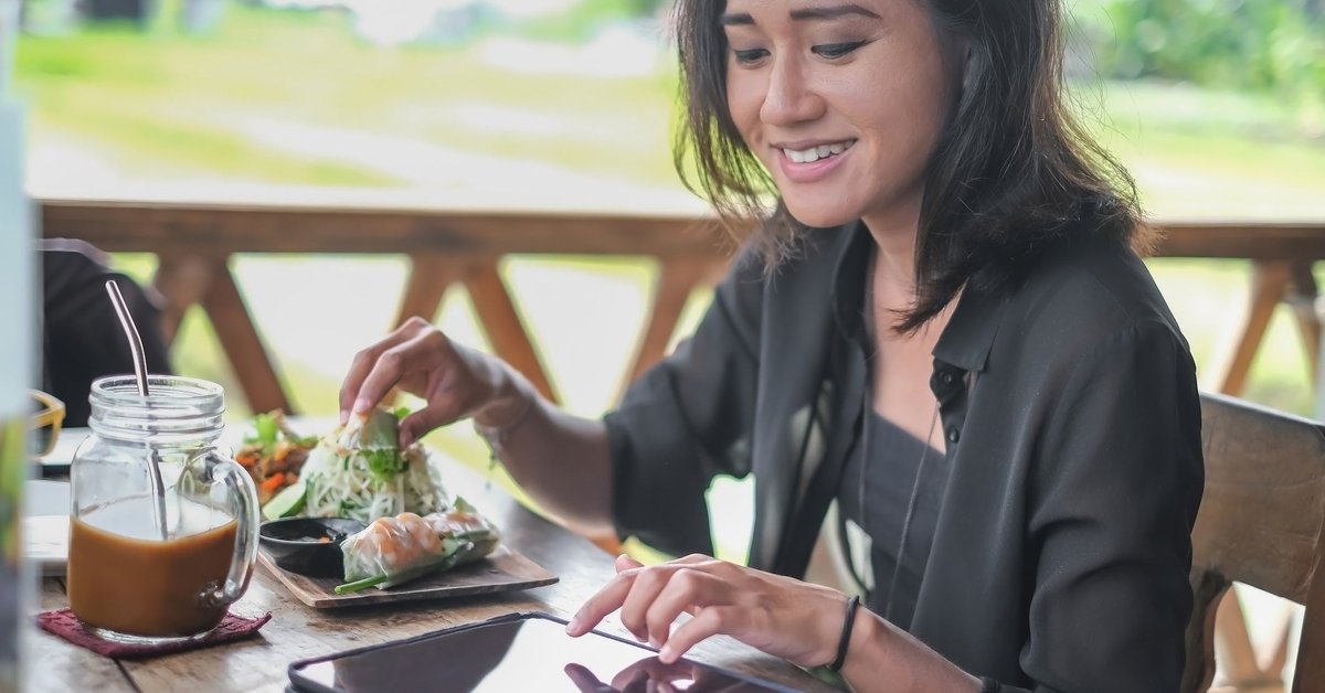 Someone happily uses a smart tablet while eating at a cafe outside.