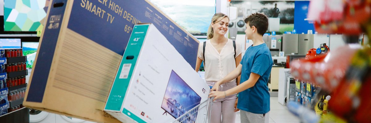 Woman and child pushing cart loaded with two flat screen tvs inside electronics store.