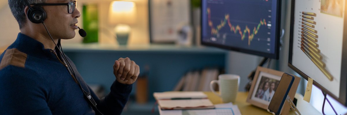 A cryptocurrency trader wearing a headset is on a video call from a home office.