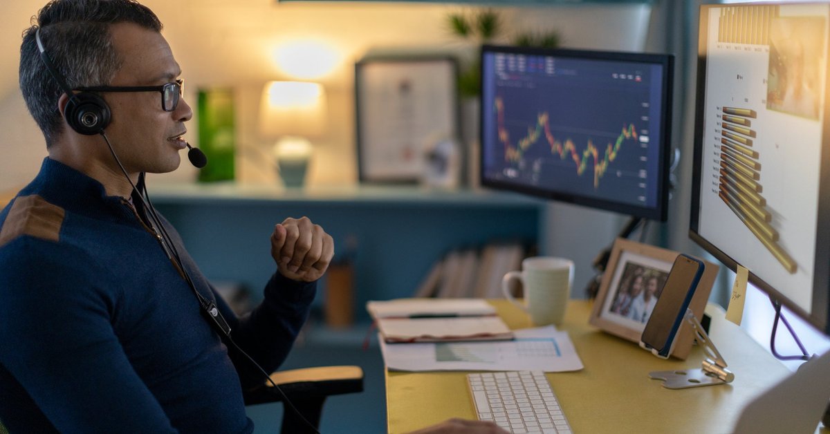 A cryptocurrency trader wearing a headset is on a video call from a home office.