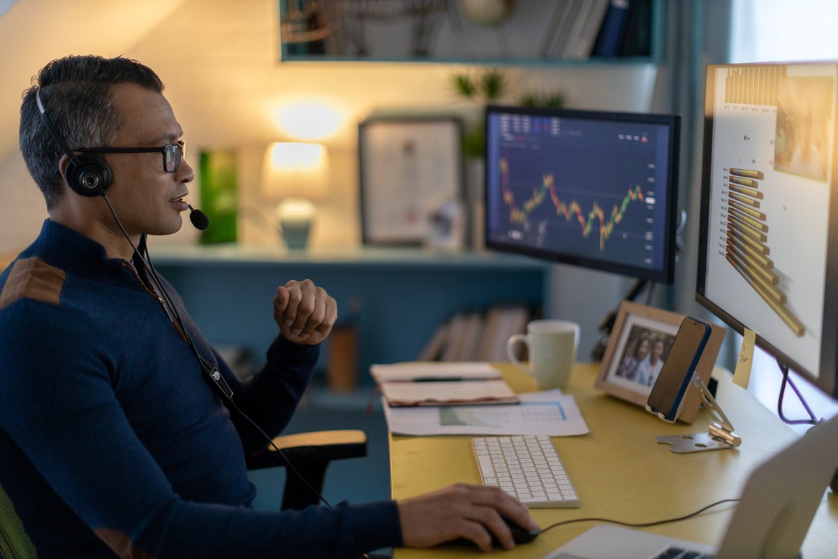 A cryptocurrency trader wearing a headset is on a video call from a home office.