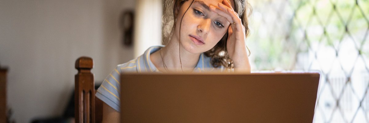A worried young adult uses a laptop at home.