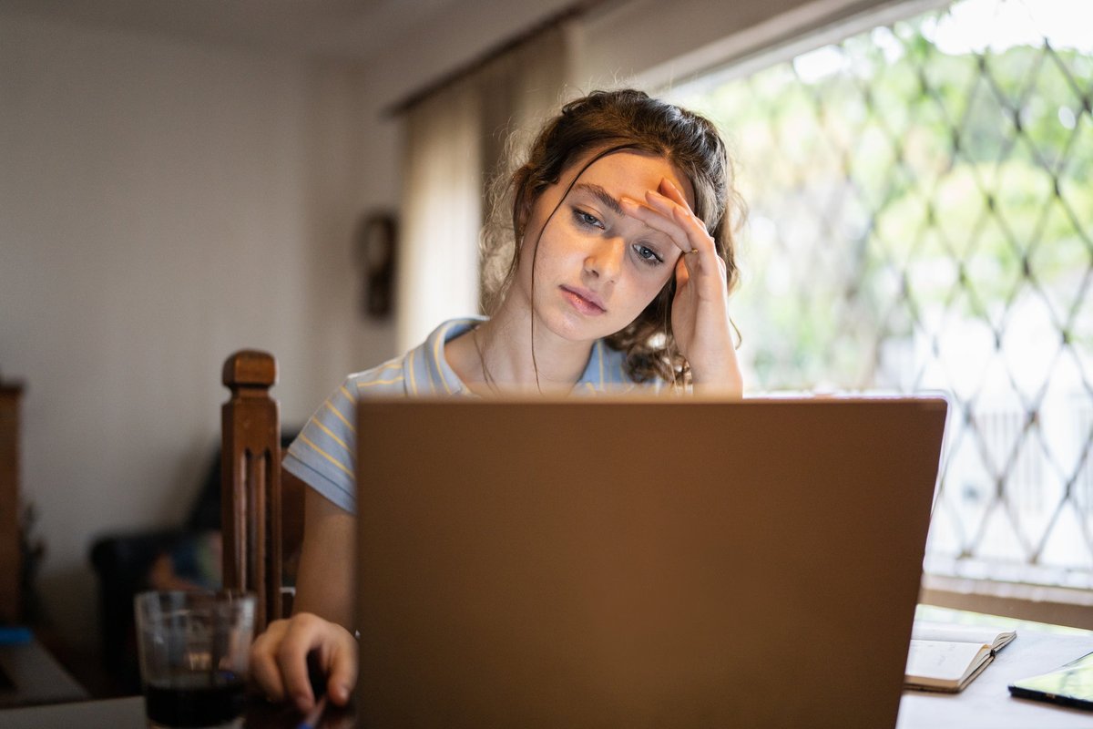 A worried young adult uses a laptop at home.