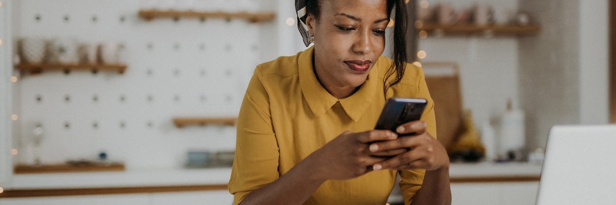 An adult with a neutral expression uses their smartphone in their kitchen.