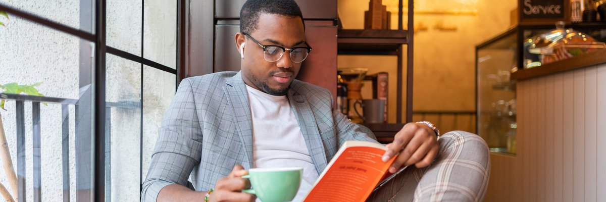 Person reading a book, drinking coffee, and listening to ear buds.