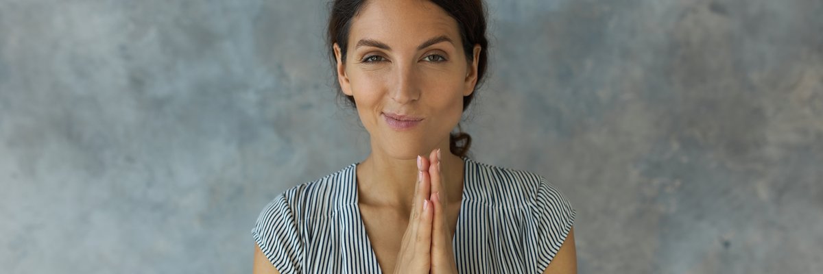 Woman smirking with her hands together in front of her chest.