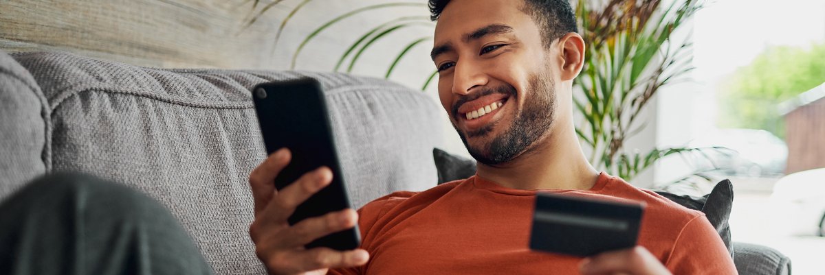 Person smiles while holding credit card and looking at cellphone.
