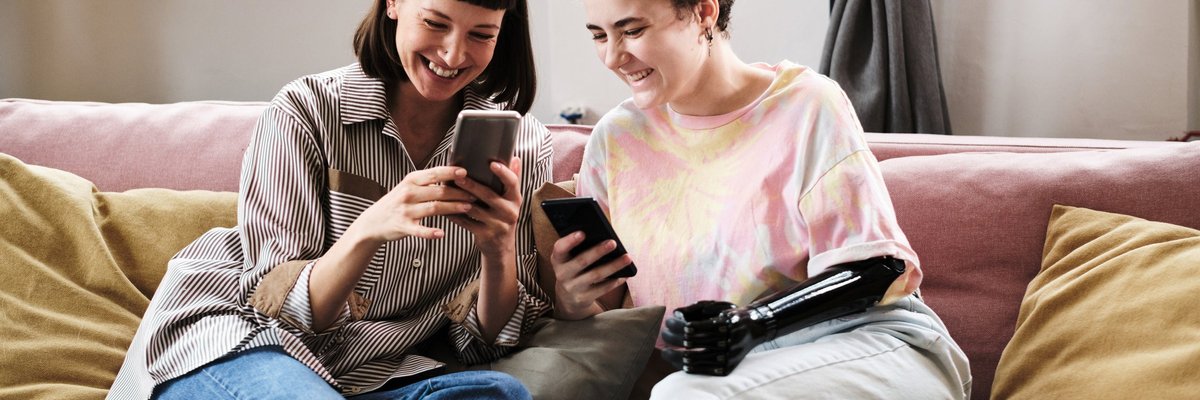 An interabled couple looks at their smart phones excitedly while sitting on a couch.