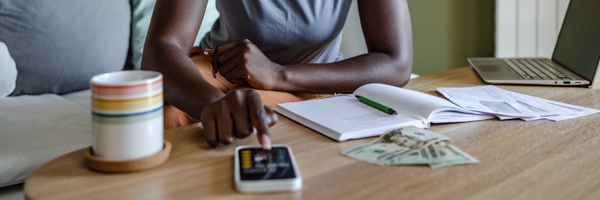 Woman makes calculations on her phone with open notebook nearby.