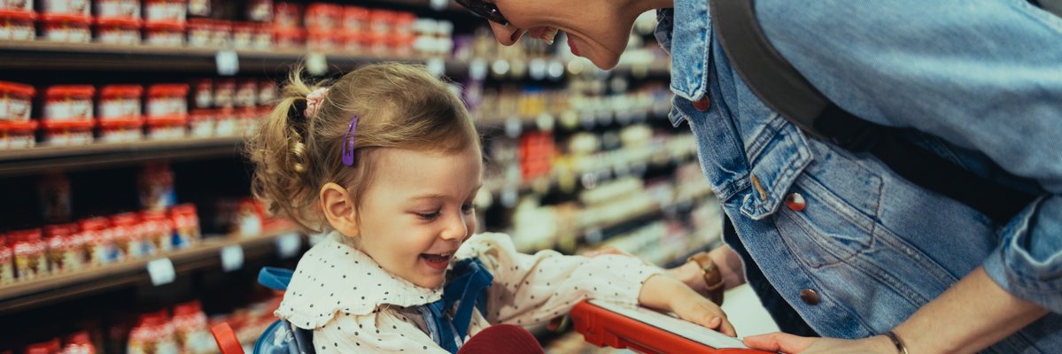 Toddler in shopping cart with parent at the grocery store.