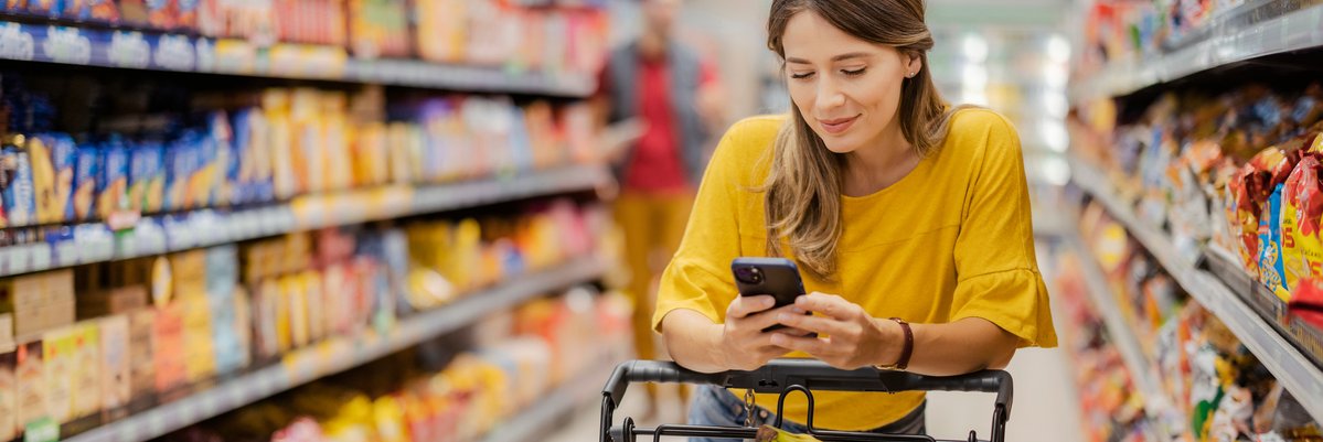 Woman pushing full cart down grocery store aisle.