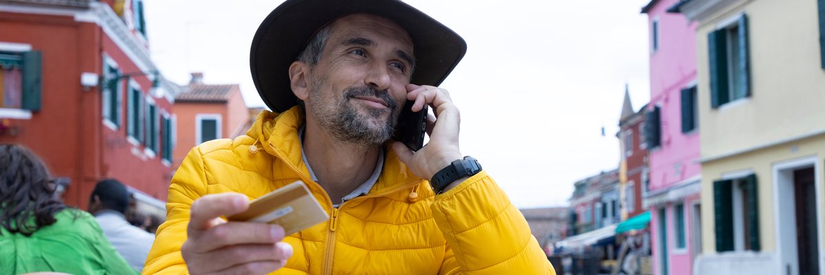 Traveler holds credit card and talks on phone at outdoor cafe.