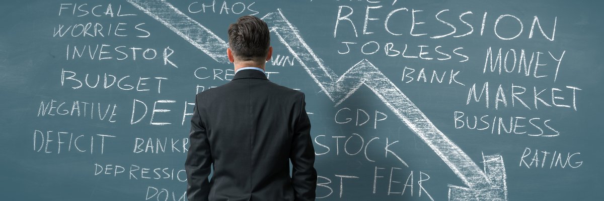 Man facing chalkboard featuring a downward trending arrow and words and phrases relating to a recession.
