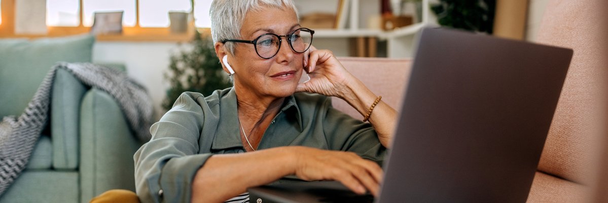 Mature woman using laptop with earbuds in.