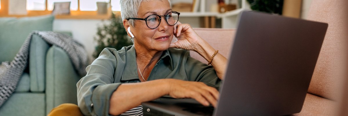 Mature woman using laptop with earbuds in.
