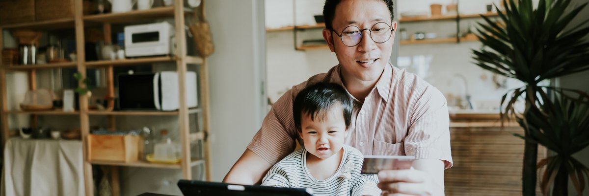 Father and toddler using tablet at table and smiling while holding credit card.